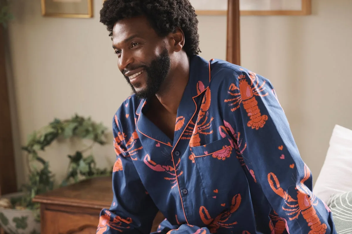 Người đàn ông mặc bộ pyjama xanh hoạ tiết tôm hùm đỏ, ngồi trên giường.